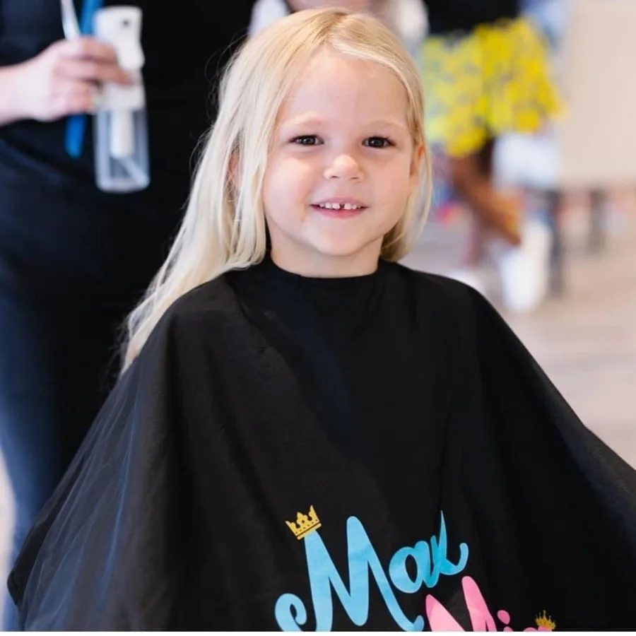 Smiling girl in a Max & Mia salon cape after her haircut